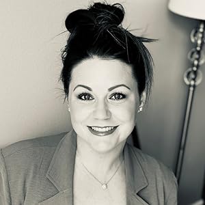 Black and white portrait of Brittany Roth, smiling, with hair styled in a bun and wearing a blazer. A lamp is visible in the background.