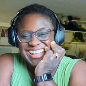 Denise Twum, smiling while wearing headphones and a green shirt in a cozy workspace.